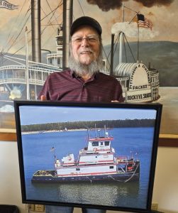 Chuck Piepmeier, retired information systems manager for McGinnis Inc., stands with a painting of his namesake vessel. (Photo courtesy ofMcGinnis Inc.)
